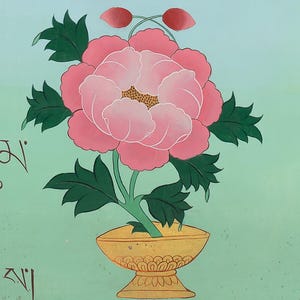 May include: A hand-painted floral artwork featuring a large pink peony in a gold vase, with green leaves and two red buds. The background is a light teal colour with Tibetan script and a red vertical stripe.