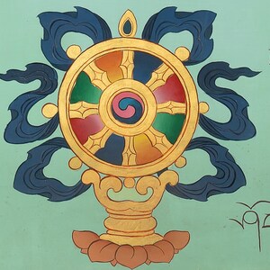 May include: A hand-painted Dharma Wheel, a Buddhist symbol, in vibrant colours. The wheel has red, green, yellow, and blue segments, with a central swirl. Dark blue ribbons and gold detailing are also present.