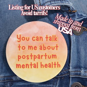 Pode incluir: Um botão redondo com um design em aquarela em tons de pêssego e amarelo. O botão tem o texto "You can talk to me about postpartum mental health" em laranja. O botão está em uma jaqueta jeans.