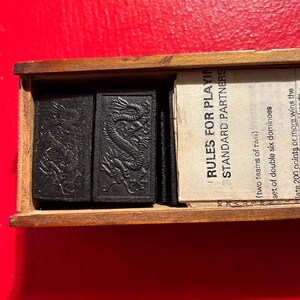 Puede incluir: Caja de madera que contiene domin&oacute;s negros con grabados de dragones. La caja tambi&eacute;n contiene un folleto con el texto "RULES FOR PLAYING STANDARD PARTNERS". Un juego cl&aacute;sico.
