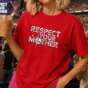 May include: A bright red short-sleeved t-shirt featuring the text "RESPECT YOUR MOTHER" printed in a silver, glittery, diamond-like font. The letter "O" in "MOTHER" is replaced by a sparkling disco ball graphic with radiating light beams.