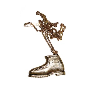 May include: A gold chain necklace with a gold boot pendant. The boot is detailed with stitching and a small rectangular tag.