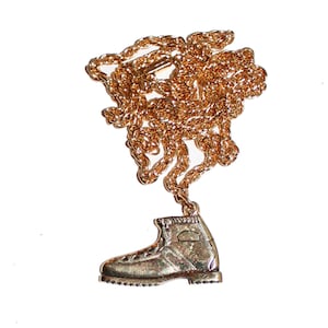 May include: A gold chain necklace with a gold boot pendant. The chain is a rope style and the boot is detailed with stitching.
