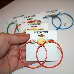 May include: Two pairs of orange hoop earrings on a white card with the text "JOE BOXER" printed on it. The earrings are on a white card with the text "JOE BOXER" printed on it.
