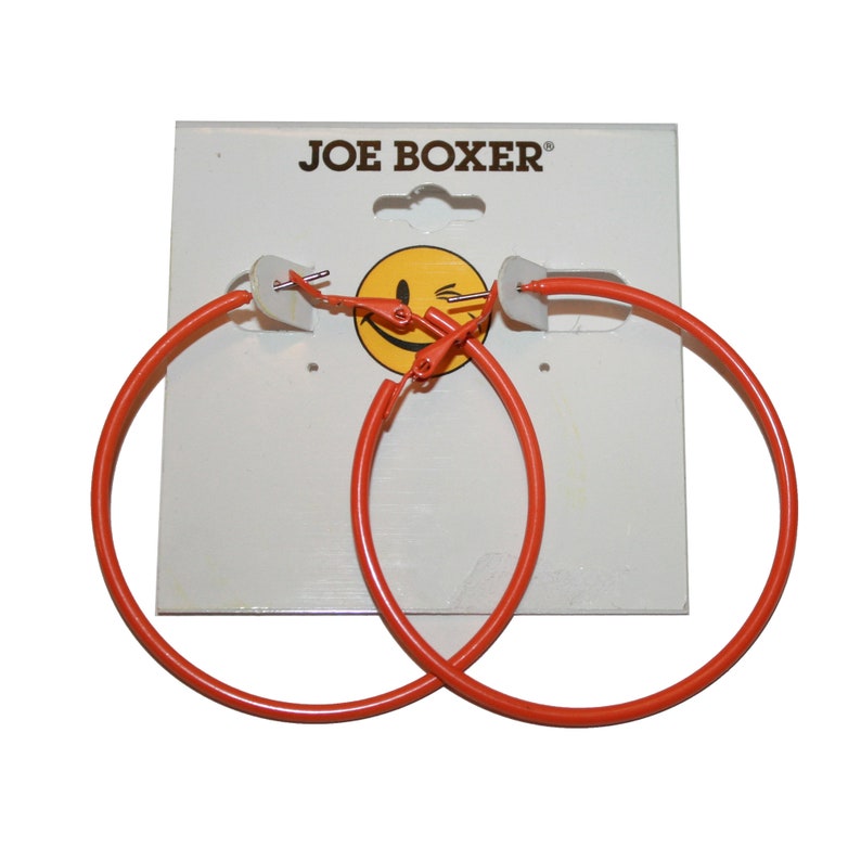 May include: A pair of orange hoop earrings with a silver clasp. The earrings are on a white card with the text "JOE BOXER" printed on it.