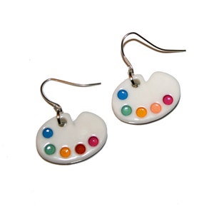 May include: A pair of white ceramic earrings shaped like artist's palettes with colourful paint dots.