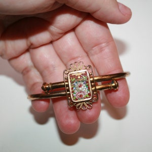 May include: Gold-toned bracelet with a rectangular, mosaic-style centerpiece. The centerpiece features a floral design with red, white, and green elements. The bracelet has a double-bar design with decorative end pieces.