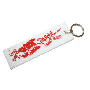 May include: White rectangular keychain with red text and a metal ring. The text reads "I love being in S-A-D-E, it's EXERCISE, I CAN'T STAND!" The keychain has a hole for the ring.