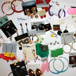 Puede incluir: Una colecci&oacute;n de varios pendientes de moda, incluyendo aros, tachuelas y estilos colgantes. Los pendientes son de varios colores, materiales y dise&ntilde;os, algunos a&uacute;n en sus tarjetas de exhibici&oacute;n originales.