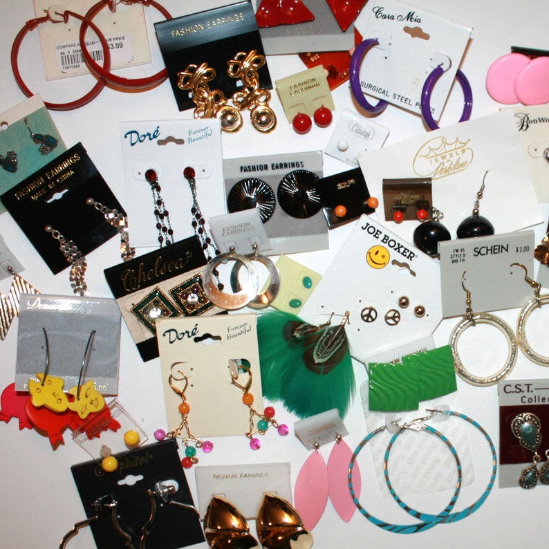 Puede incluir: Una colecci&oacute;n de varios pendientes de moda, incluyendo aros, tachuelas y estilos colgantes. Los pendientes son de varios colores, materiales y dise&ntilde;os, algunos a&uacute;n en sus tarjetas de exhibici&oacute;n originales.