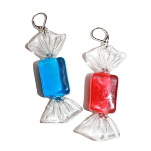 May include: A pair of candy-shaped earrings. One earring is blue and the other is red. The earrings are made of glass and have a silver hook.