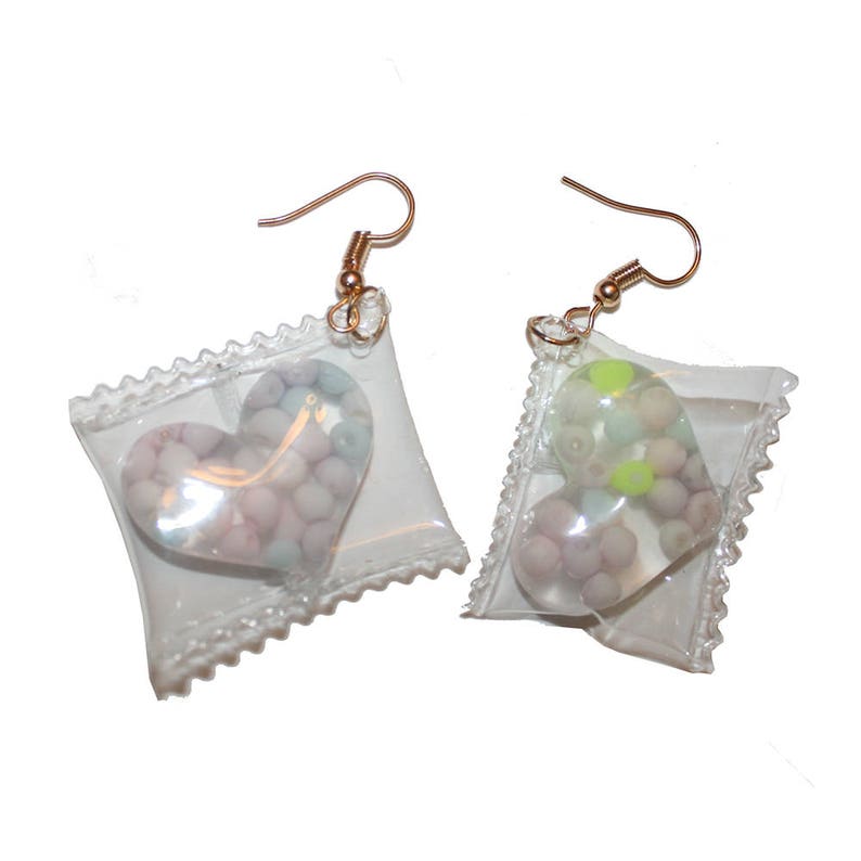May include: A pair of gold earrings with clear plastic pouches containing heart-shaped candy. The candy is pink, white, and blue in one pouch and pink, white, and green in the other pouch.