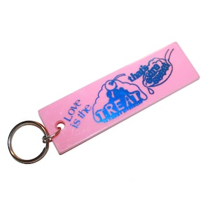 May include: Pink rectangular keychain with a silver key ring. The keychain has blue text and graphics that read "Love is the TREAT that's extra sweet". The graphic includes a cherry and a scoop of ice cream.