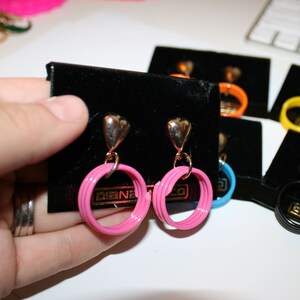 May include: A pair of pink heart-shaped dangle earrings with gold accents. The earrings are on a black velvet background with the word "Diane" printed on the card.