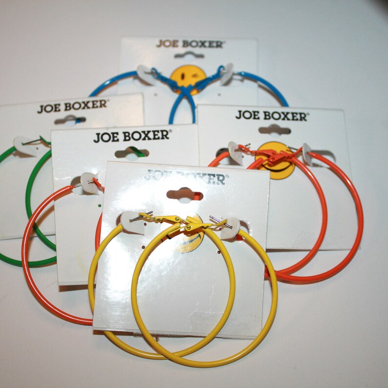 May include: Five pairs of hoop earrings on display cards. The earrings are in various colors: green, orange, yellow, and blue. Each card has the brand name "JOE BOXER" printed on it.