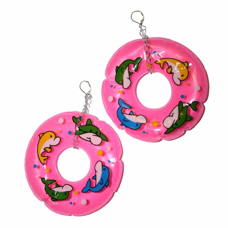 Puede incluir: Pendientes de aro hinchable rosa con dise&ntilde;o de delfines. Los aros son transl&uacute;cidos y tienen una cadena plateada.
