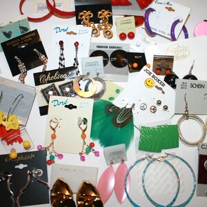 Puede incluir: Una colecci&oacute;n de pendientes de moda en tarjetas blancas, que incluyen dise&ntilde;os dorados, plateados y coloridos. Los estilos incluyen aros, colgantes y tachuelas. Algunos pendientes tienen el texto "Fashion Earrings", "Chelsea" y "Dor&eacute;".