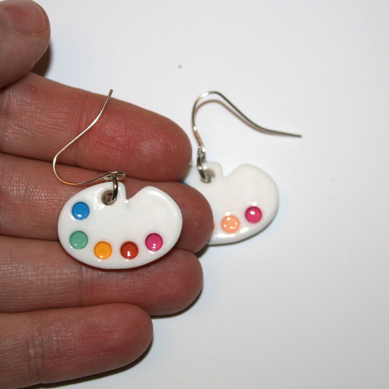 May include: A pair of white ceramic earrings shaped like artist's palettes with colourful paint dots.