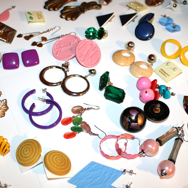 Puede incluir: Una colecci&oacute;n de pendientes vintage en varios estilos y colores, incluyendo aros, tachuelas y pendientes colgantes. Los pendientes est&aacute;n hechos de diferentes materiales, como metal, pl&aacute;stico y cuentas. Los colores incluyen p&uacute;rpura, rosa, verde y amarillo.