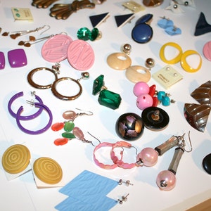 Puede incluir: Una colecci&oacute;n de pendientes vintage en varios estilos y colores, incluyendo aros, tachuelas y dise&ntilde;os colgantes. Los pendientes presentan una gama de materiales, como metal, pl&aacute;stico y piedras preciosas. Los colores incluyen rosa, morado, verde y amarillo.
