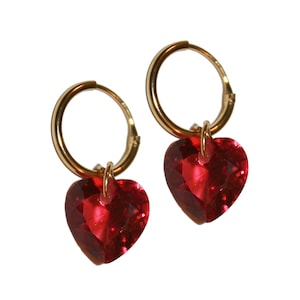 May include: Gold hoop earrings with dangling red heart-shaped crystal charms.