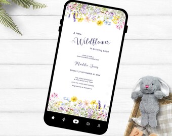 May include: A smartphone shows a baby shower invitation with a floral design. The invitation text reads "A little Wildflower is arriving soon" and includes details for Maddie Jones' baby shower. A plush bunny and wooden blocks are in the background.