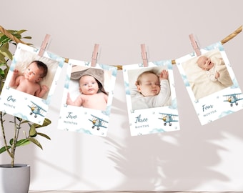 May include: Four baby milestone photo cards clipped to a rope with wooden clothespins. Each card features a baby photo, a blue airplane graphic, and the month number. The cards are labeled "One Month", "Two Months", "Three Months", and "Four Months".