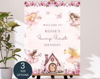 May include: A pink and white welcome sign for a first birthday party. The sign features illustrations of fairies, butterflies, and a pink house. Text reads "Welcome to Rosie's Fairy First Birthday". The sign is displayed on a wooden easel.
