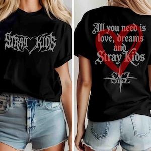 Op de afbeelding: Zwart t-shirt met de tekst "Stray Kids" in een gestileerd lettertype en een hartontwerp. De achterkant van het shirt toont de tekst "All you need is love, dreams and Stray Kids" met een hartafbeelding en de letters "SKZ".
