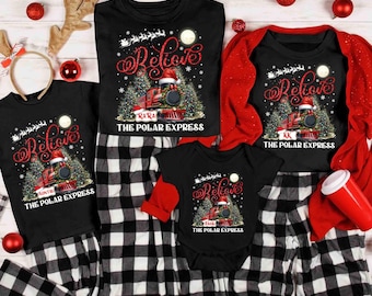 May include: A collection of black family Christmas pajamas with a "Believe" design. The design features a train, Santa hat, and Christmas trees. The pajamas include long-sleeved shirts and pants in a black and white plaid pattern. Red accents are present.