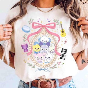 May include: Cream-colored t-shirt featuring a cartoon design of cute, colorful animals inside a pearl-framed oval. The design includes musical notes, a pink bow, a guitar, and the text "NMIXX".