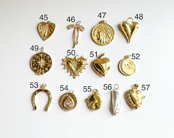 Könnte beinhalten: Eine Sammlung goldfarbener Anhänger und Kettenanhänger, darunter Herz-, Münz- und Hufeisenformen. Einige Anhänger weisen aufwendige Details wie eine Windrose, eine Schleife und einen birnenförmigen Edelstein auf. Die Anhänger werden vor weißem Hintergrund präsentiert.