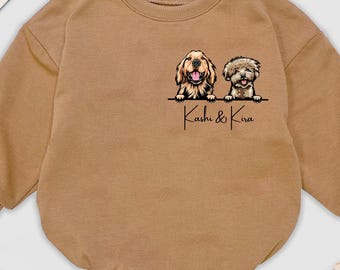 Puede incluir: Un body de bebé color canela con mangas largas. El body presenta un gráfico de dos perros y el texto "Kashi & Kira". La palabra "BABY" está escrita con letras de madera.