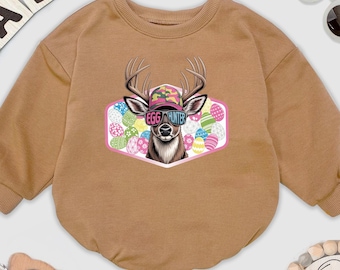May include: A tan baby romper with long sleeves. The front features a graphic of a deer wearing a camouflage hat and sunglasses, with the text "Egg Hunter." The background includes colorful Easter eggs. Baby-themed items surround the romper.