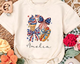 May include: Cream-colored baby bodysuit with a patriotic graphic featuring an ice cream cone, bows, and a hot dog, all in red, white, and blue. The name "Amelia" is written in script below the graphic.
