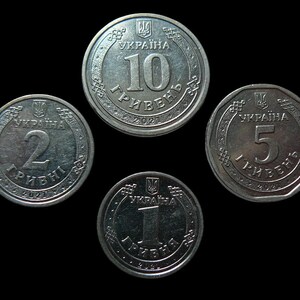 May include: Four Ukrainian coins of different denominations are displayed against a black background. The coins are silver-colored and feature the Ukrainian coat of arms and Cyrillic text. The denominations are 1, 2, 5, and 10.