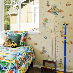 May include: A child's bedroom with a space theme. The bed has a colorful comforter and pillows. Wall decals include rockets, planets, and astronauts. A height chart is on the wall, and a blue coat rack with a toy truck on top.