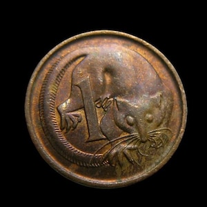 May include: A bronze-coloured Australian one-cent coin. The coin shows a stylised depiction of a squirrel-like animal, with the number "1" clearly visible. The coin is circular and set against a black background.