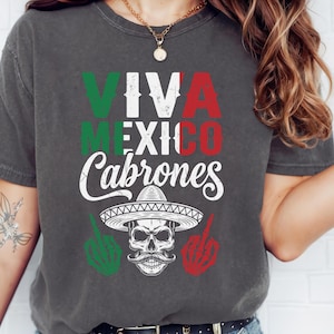 May include: Dark gray t-shirt with the words "VIVA MEXICO Cabrones" in green, red, and white. The design includes a skull wearing a sombrero and skeleton hands giving the middle finger.