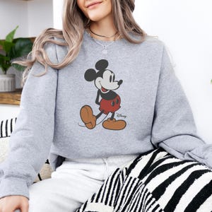 Puede incluir: Sudadera gris claro con un gr&aacute;fico de Mickey Mouse. El personaje de dibujos animados est&aacute; en negro, rojo y marr&oacute;n, con el logotipo de Disney. La sudadera es de estilo casual.
