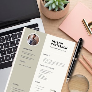 May include: A software developer's CV, featuring Nelson Patterson's details, including a photo, education, and skills. A black pen, a pink notepad with a gold clip, a magnifying glass, and a laptop are on a wooden surface.