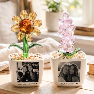 May include: Two decorative flower sculptures in white pots. One is a sunflower with yellow and orange crystal petals, the other is a pink crystal flower. Each pot has a black and white photo and the words "Soul Sister Forever" and "Bestie Forever".