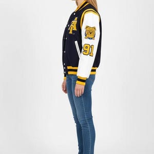 May include: Navy blue and white varsity jacket with yellow accents. Features a bulldog patch and the number 91 on the sleeve. The jacket has a button-up front and is worn with blue jeans and white sneakers.