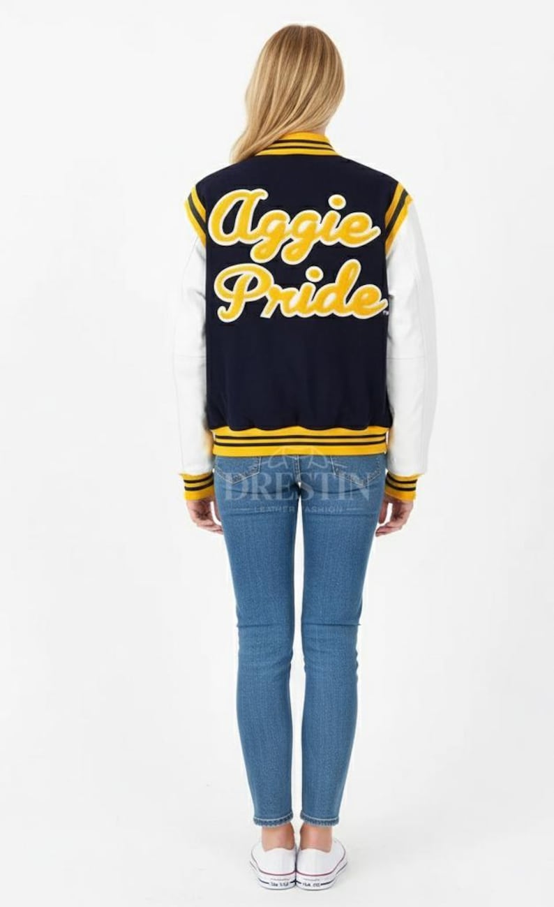 May include: A navy blue and white letterman jacket with the words "Aggie Pride" in yellow script on the back. The jacket has yellow and white striped accents and is worn with blue jeans and white sneakers.