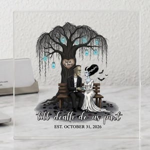 Puede incluir: Una placa cuadrada de acrílico transparente con una ilustración impresa de Frankenstein y su novia sentados en un banco bajo un sauce con linternas colgantes. El texto dice "Sarah & David", "Till death do us part" y "EST. OCTOBER 31, 2026".
