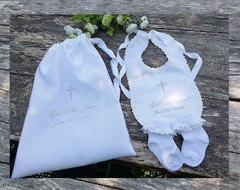 Peut inclure: Un sac en satin blanc avec cordon de serrage, une croix argentée et le texte "God Bless Ava June 24, 2023". Une bavette de bébé blanche avec bordure en dentelle et une croix argentée, avec le texte "God Bless Ava June 24, 2023".