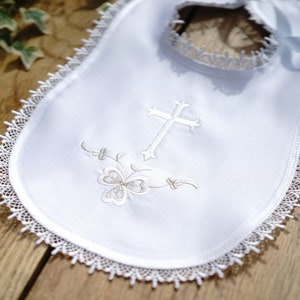 May include: White baby bib with a delicate lace trim and a cross and floral embroidery. The bib has a satin ribbon for tying. A beautiful baptism or christening bib.