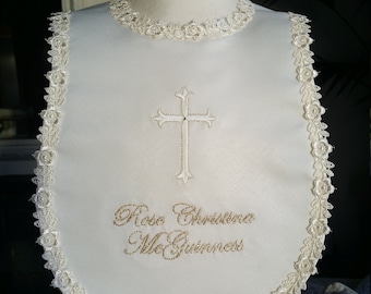 Peut inclure: Bavoir blanc avec une délicate bordure en dentelle et une croix brodée au centre. Le bavoir porte le nom brodé "Rose Christina McGuinness" en fil doré, adapté à un baptême.