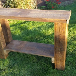 May include: A rustic wooden console table with a single shelf. The table is made of reclaimed wood and has a natural, weathered finish. The table is 30 inches tall and 36 inches wide.
