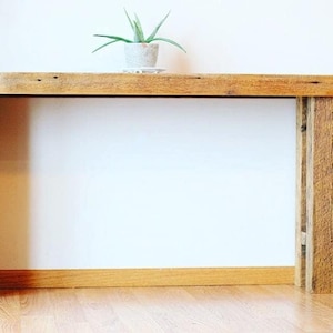 May include: A rustic wooden console table with a natural wood finish. The table has a simple design with a rectangular top and two legs on each side. The table is made of reclaimed wood and has a distressed look.